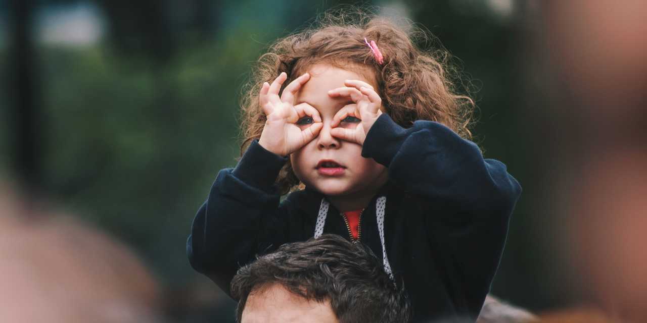 Flicka på pappas axlar kikar efter mamma
