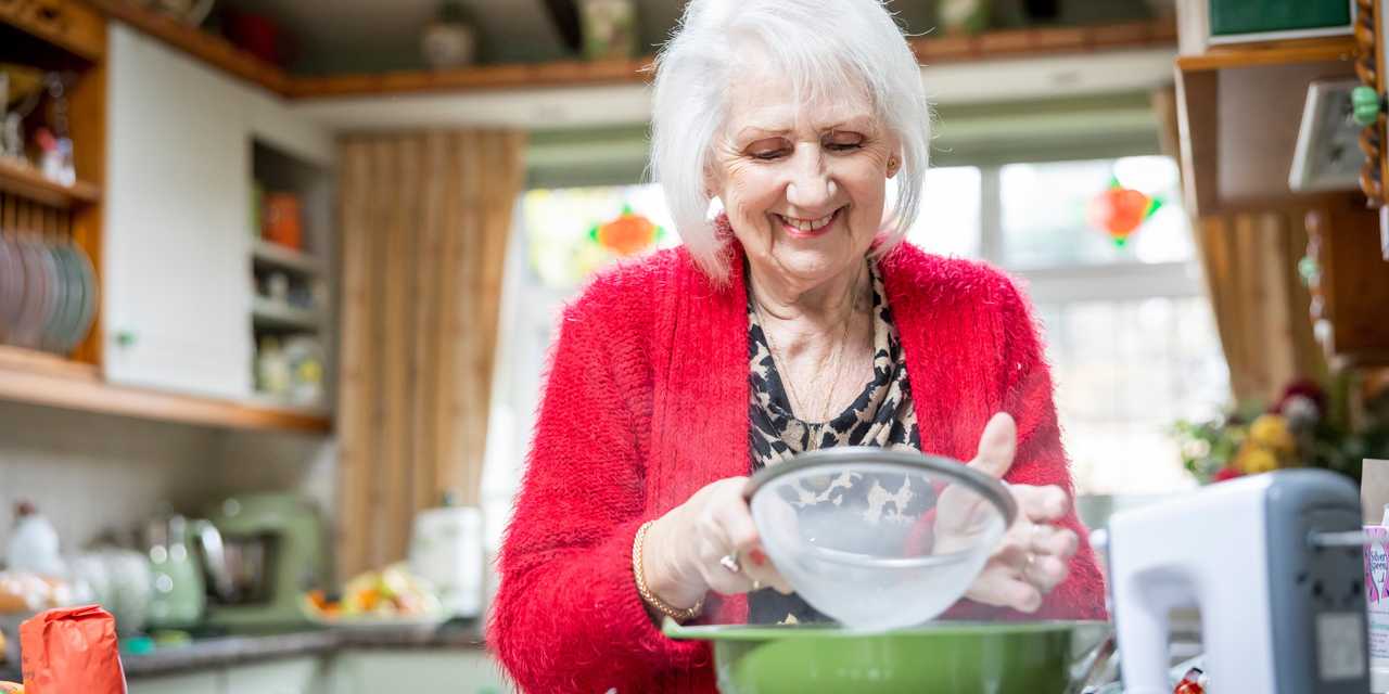 Nainen siivilöi jauhoja keittiössä