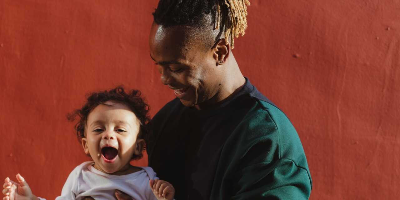 Lapsi vanhemman sylissä, punainen seinä taustalla. 