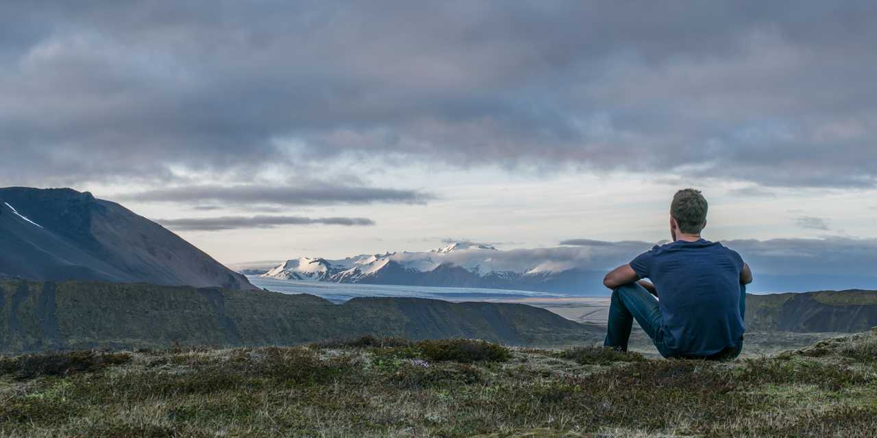 Henkilö istuu maassa, taustalla vuoria