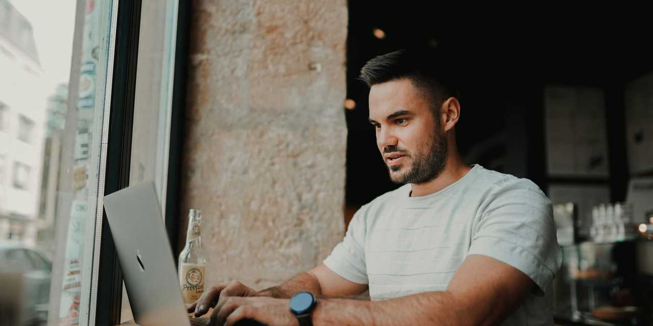 Henkilö istuu pöydän ääressä, käyttää tietokonetta.