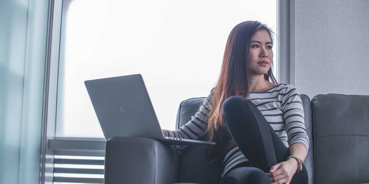 Nainen istuu läppärin kanssa sohvalla.