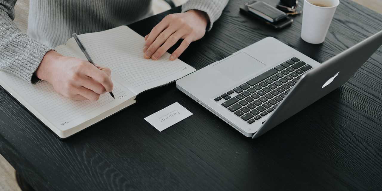 En person som sitter vid dator och med ett block framför sig