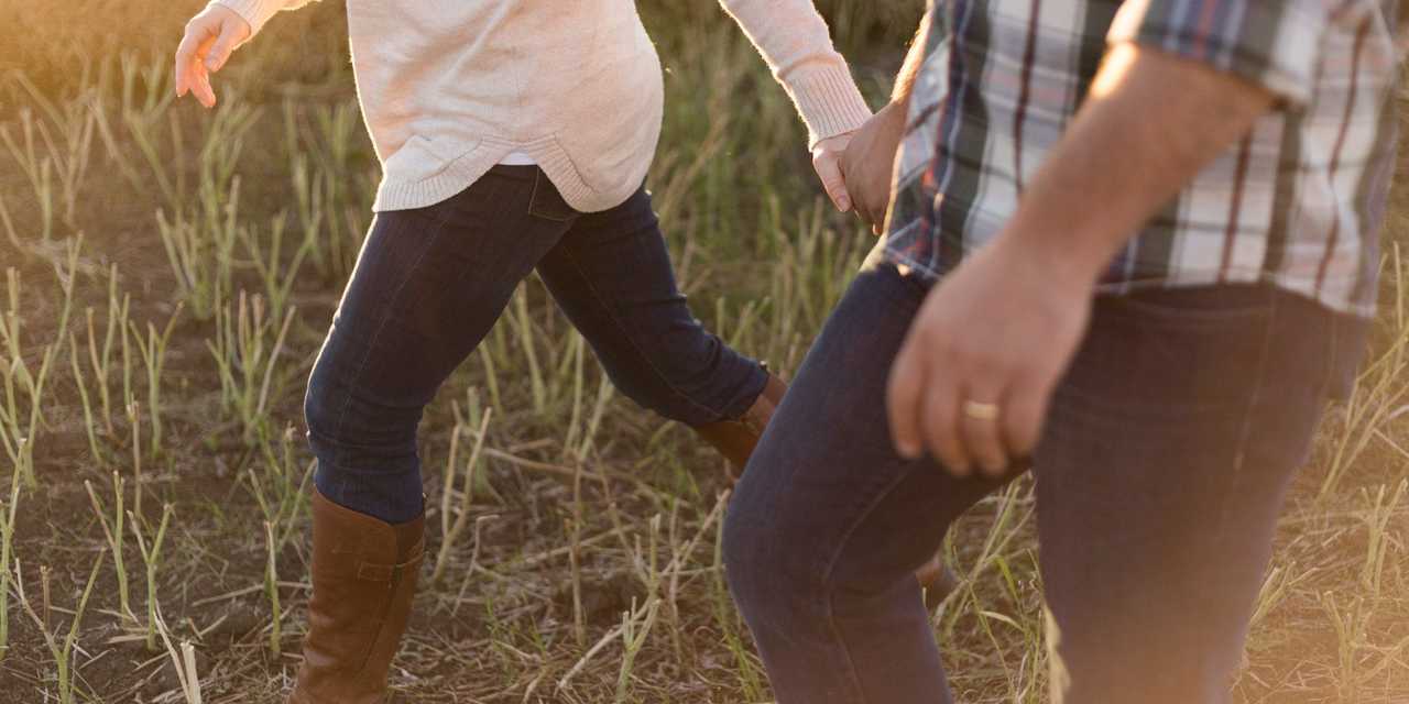 Par håller varandra i handen på en promenad i gräset